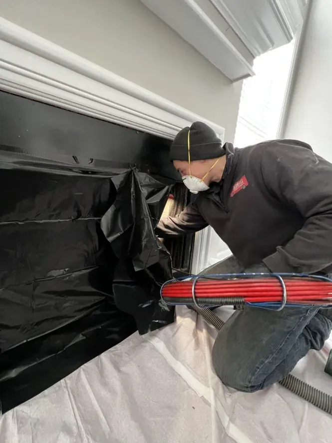 Barnhill Chimney technician performing a chimney sweep inside a Lexington home with drop cloth and equipment