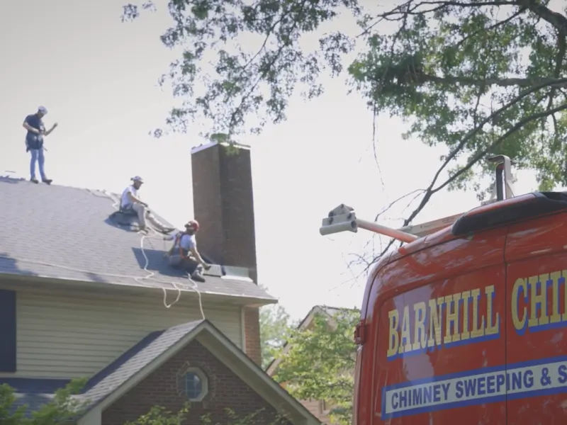 Barnhill Chimney team on a Lexington, KY rooftop inspecting a chimney for animal entry points next to the company truck